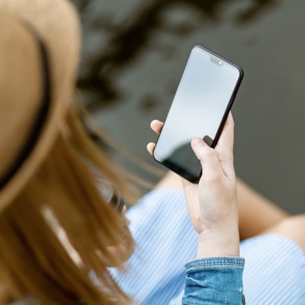 there is a photo of a girl holding a smartphone, from behind three-quarters